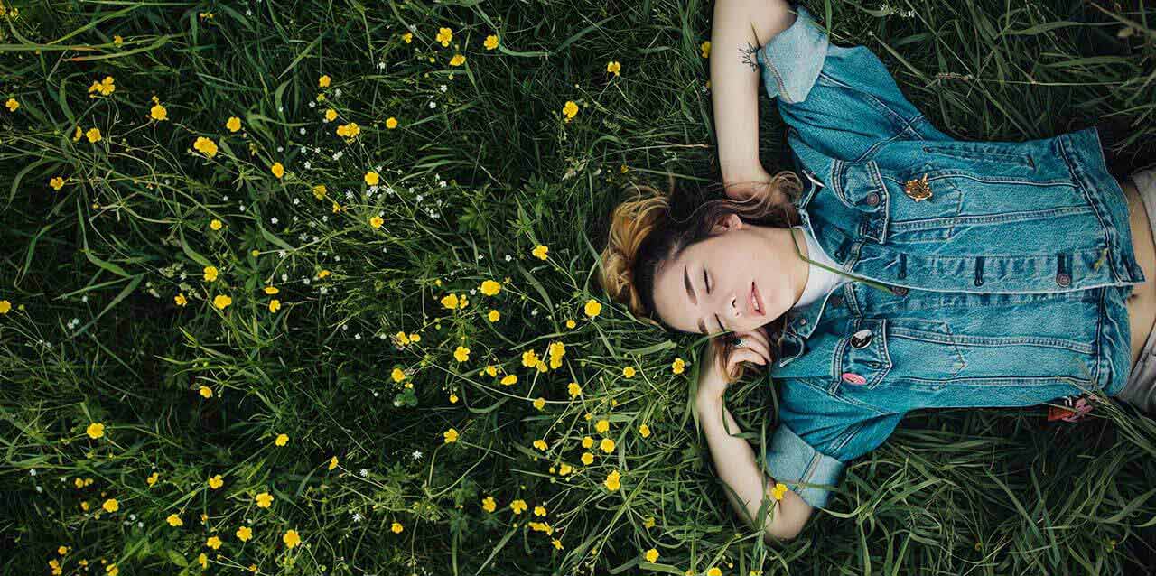 chica tumbada en cesped junto flores amarillas
