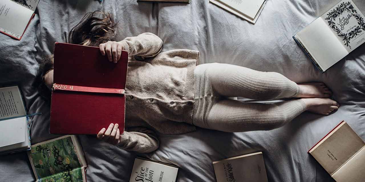 niña tumbada en cama con libros niña tumbada en cama con libros