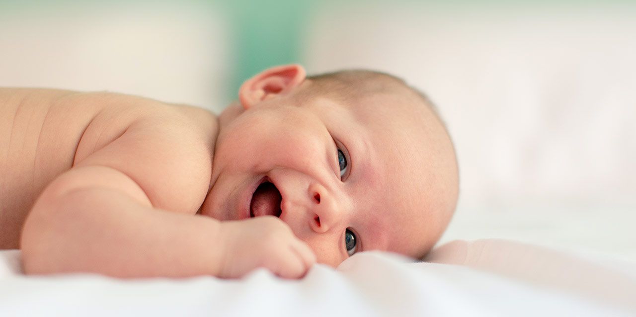 como-prevenir-la-plagiocefalia-en-los-bebes-1 bebé tumbado de lado sonriendo