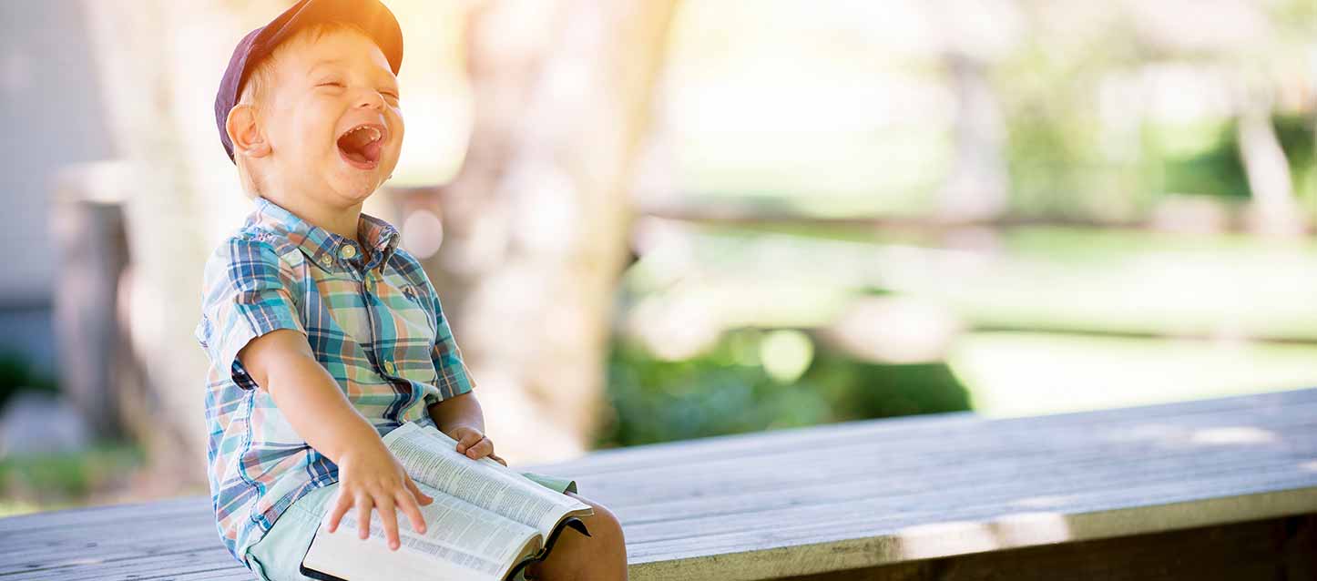 niño riendo sentado con un libro en la mano niño riendo sentado con un libro en la mano