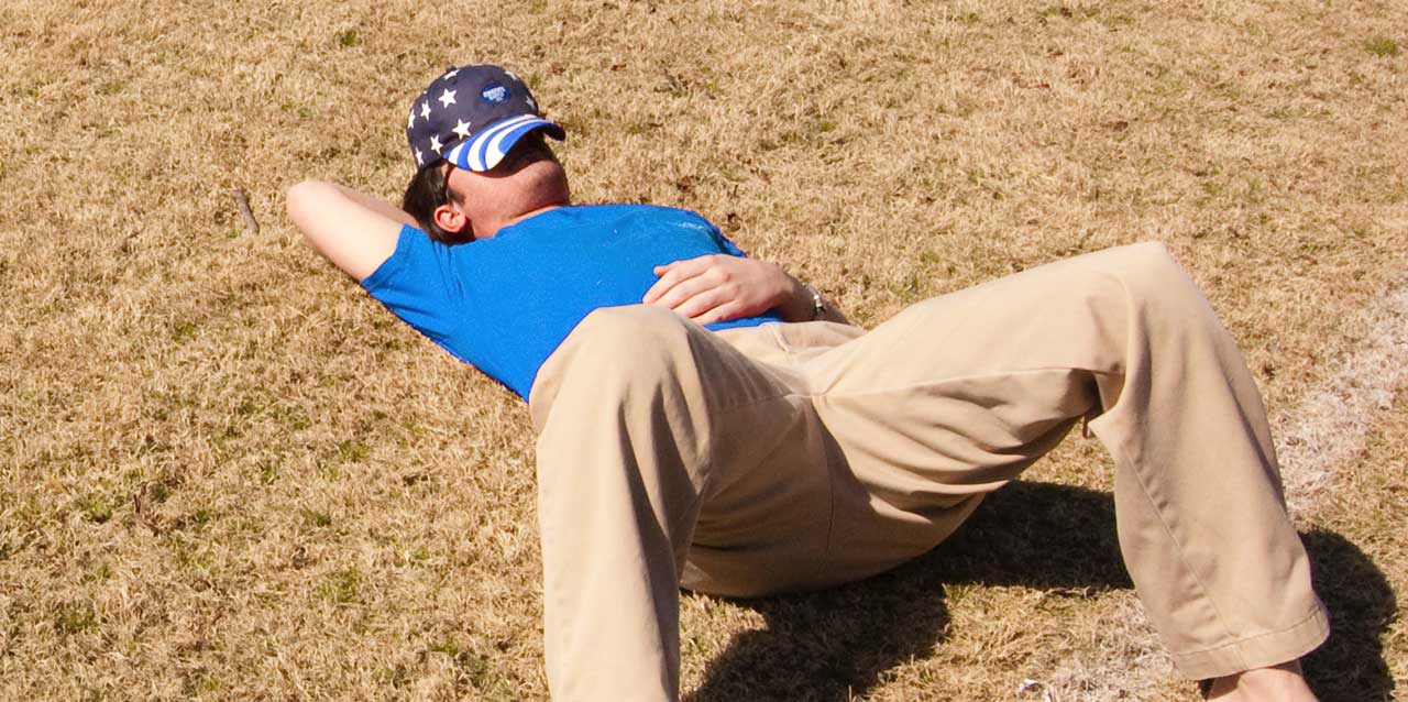 hombre tumbado en campo de fútbol con gorra en la cara