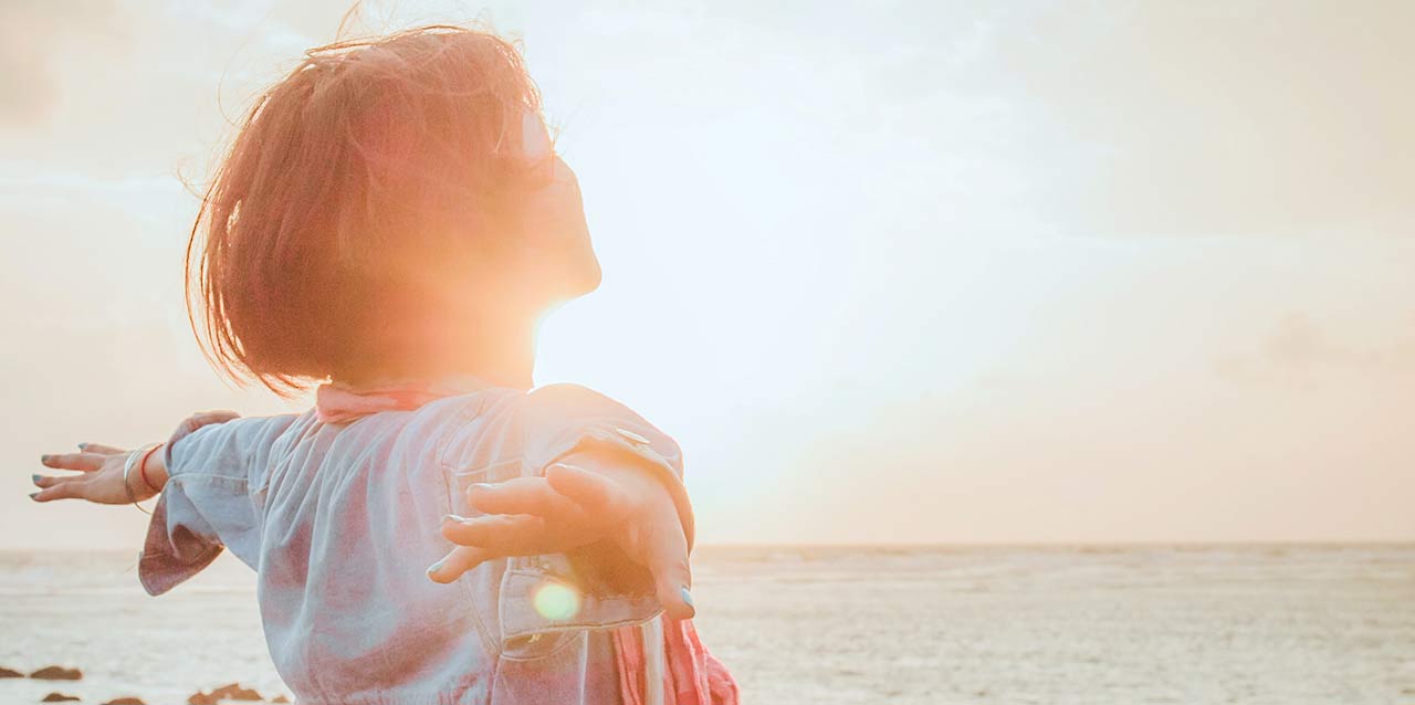 mujer con los brazos extendidos frente al mar atardeciendo mujer con los brazos extendidos frente al mar atardeciendo
