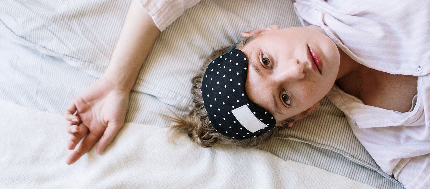 Por qué sudo si tengo frío chica con pelo castaño claro, pijama a rayas blancas y rosa y antifaz en la frente, tumbada en la cama boca arriba en la cama