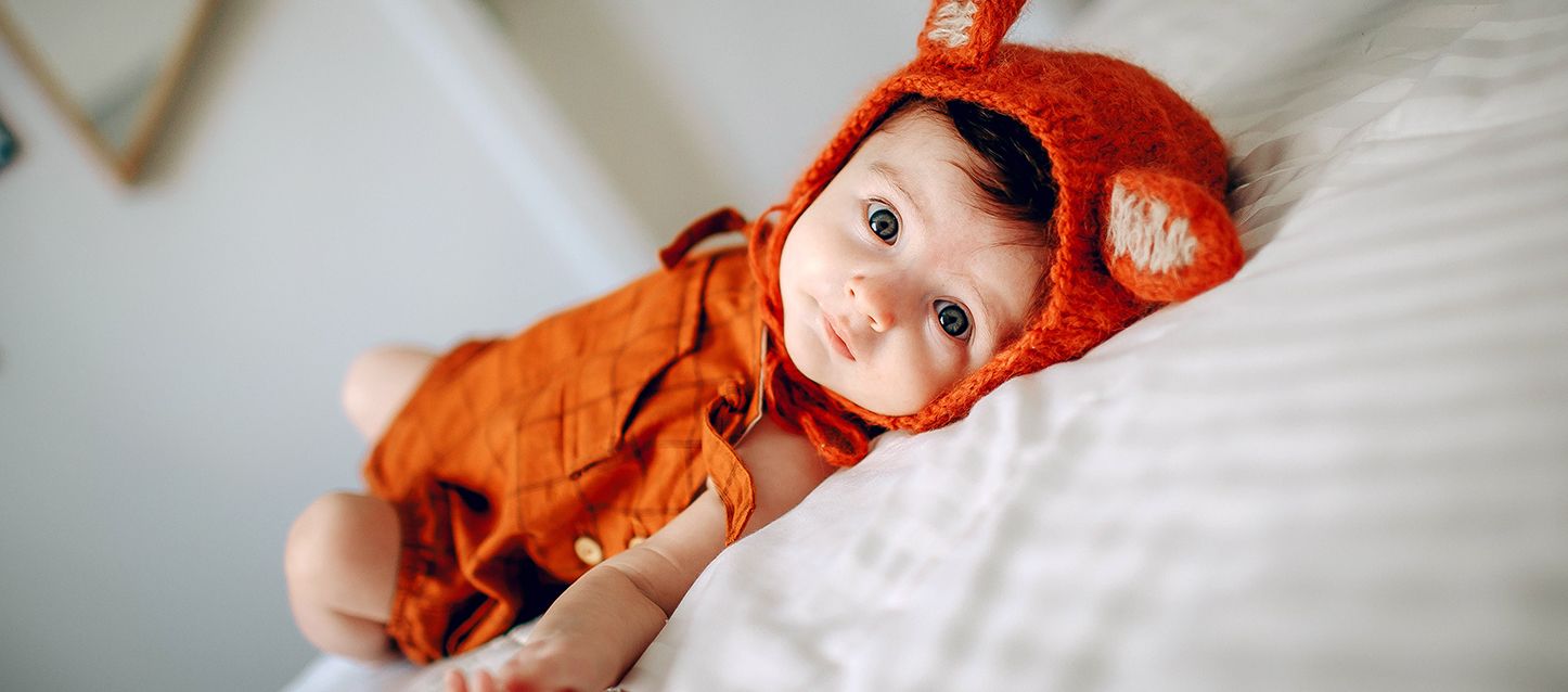 bebe de pelo negro y ojos azules con pijama naranaja y gorrito de lana naranja con orejitas