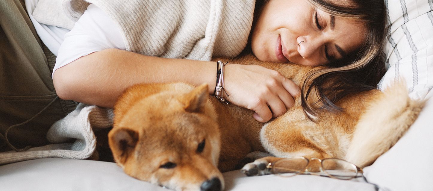 chica de pelo largo moreno y mechas rubias durmiendo de lado vestida apoyada en un perro shiba inu