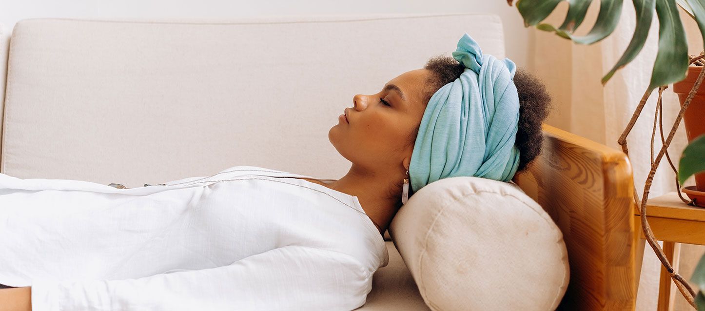 chica de piel morena y pelo afro con un turbante de color aguamarina en la cabeza durmiendo boca arriba vestida con un bluson blanco