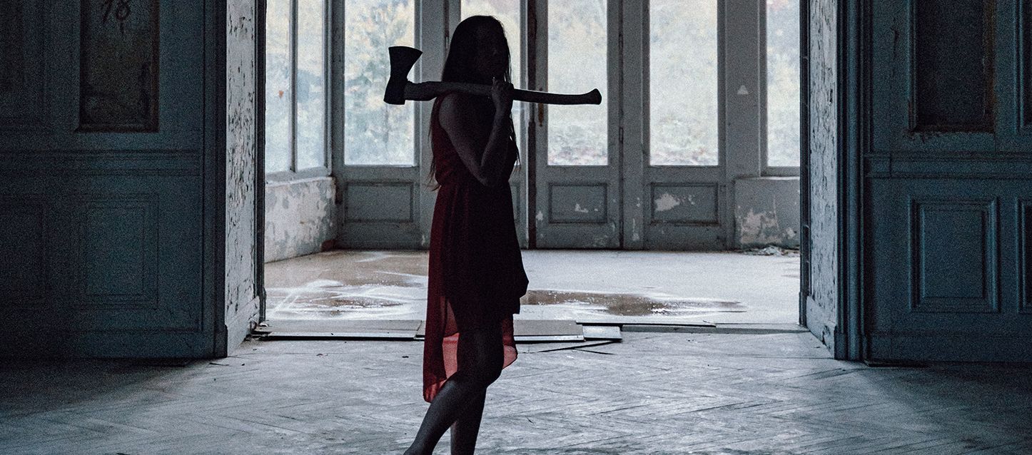 Los terrores nocturnos en adultos más frecuentes mujer de pelo largo negro de pie con vestido rojo y un hacha al hombro en una casa abandonada