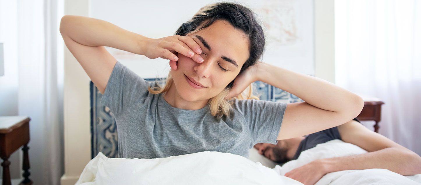 chica de pelo largo negro con mechas rubias despertando en la cama con su pareja durmiendo