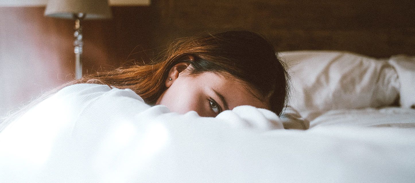 chica de pelo castaño sentada apoyada boca abajo en la cama mirando hacia un lado
