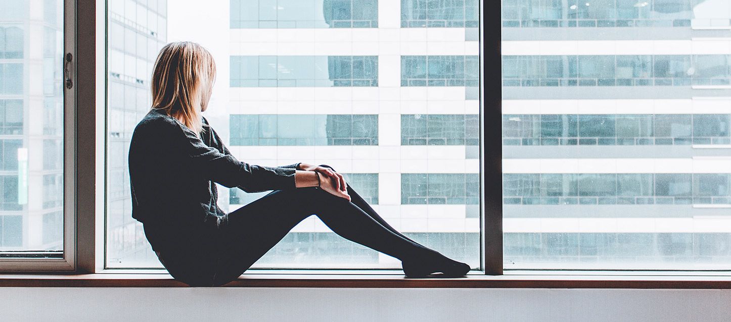 Por qué tengo ansiedad cuando me levanto chica rubia sentada en el alfeizar de un gran ventanal con vistas al edificio de enfrente