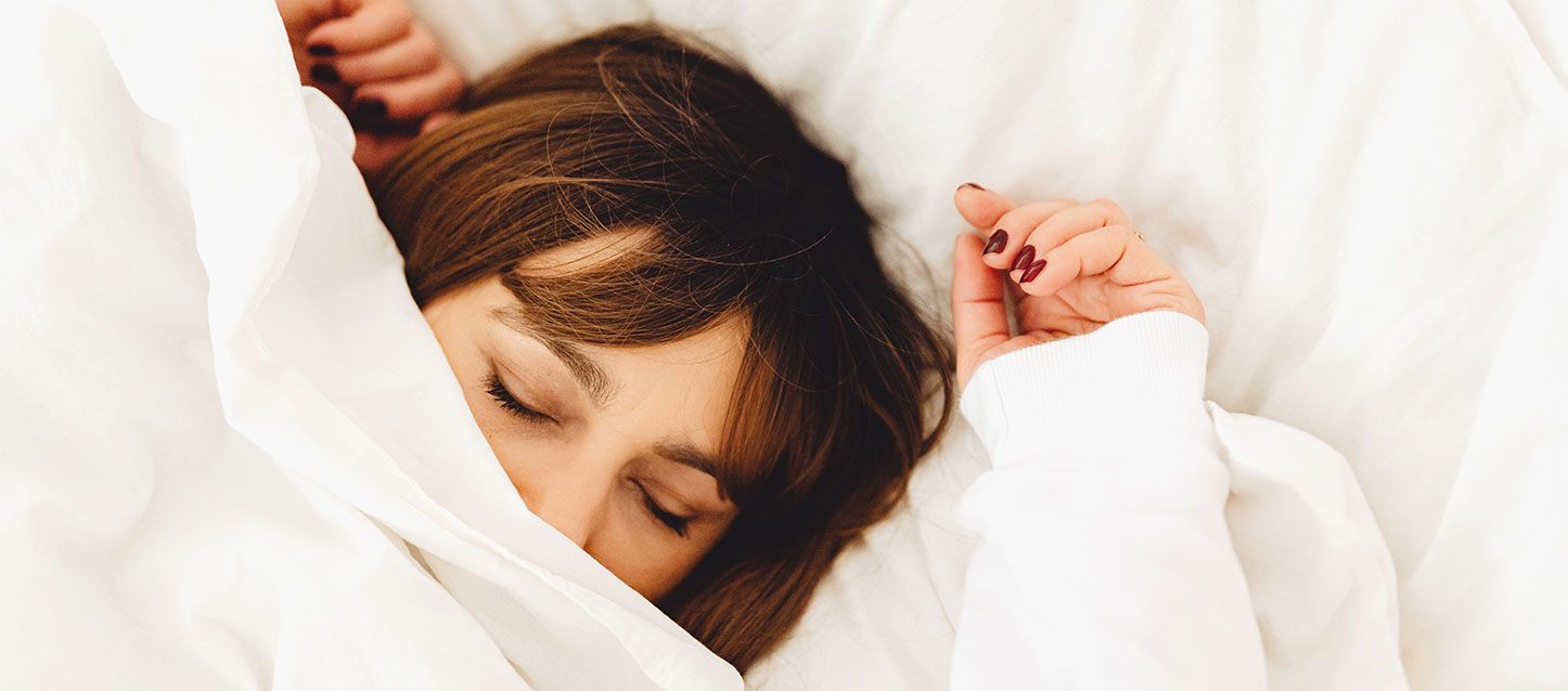 Dormir bien con alergia mujer de pelo castaño dormida dentro de la cama tapada con el edredon hasta la nariz