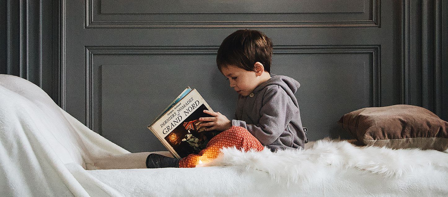 Aprender idiomas durmiendo niño pequeño sentado en una cama leyendo un libro