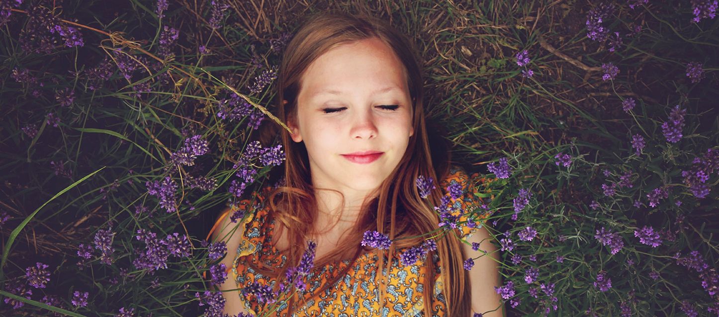 Dormir para no pensar niña de pelo largo castaño con vestido naranja y dibujos blancos tumbado boca arriba en la hierba rodeada de plantas de lavanda con los ojos cerrados
