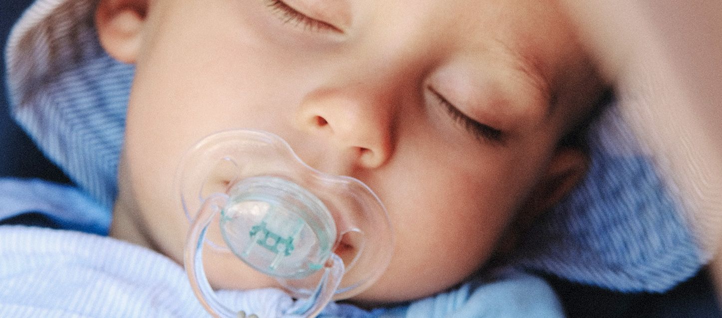¿Es bueno que un recién nacido duerma con chupete? bebe dormido boca arriba con chupete y pijamita azul