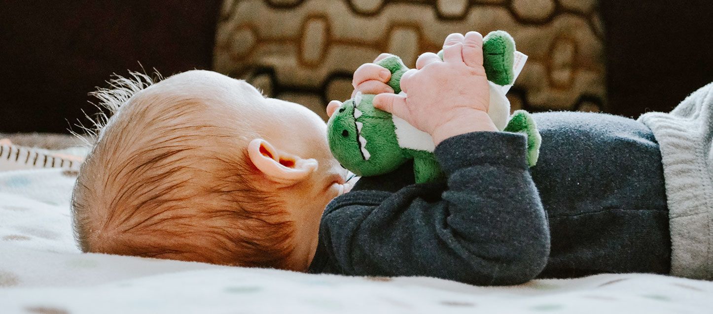 dormir con peluches bebe tumbado boca arriba con pijama de felpa negra con una dinosaurio de peluche entre las manos