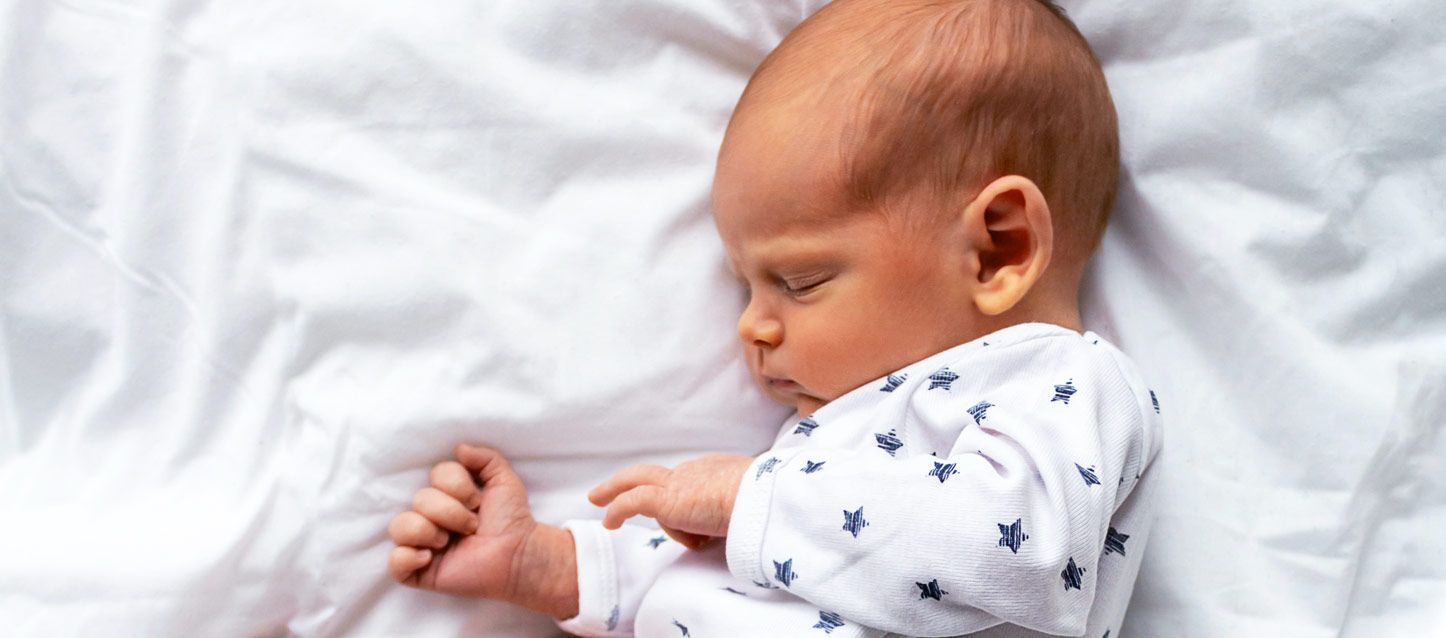 nido para bebé bebe durmiendo con pijama blanco con estrellas azules en una cama