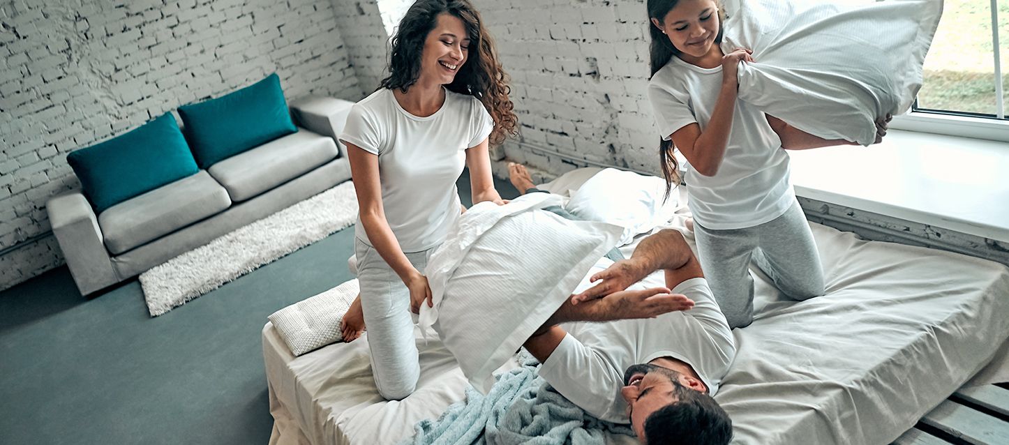 elegir el colchón perfecto 1 chico y dos chicas vestidos con pijama blanco haciendo guerra de cojines