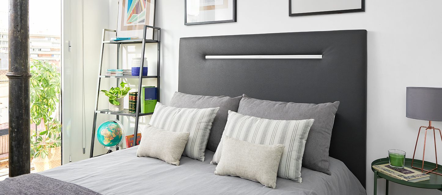 Consejos para decorar una habitación pequeña habitacion pequeña con cama, 2 almohadas y 4 cojines, estanteria con libros y mesita con una vela