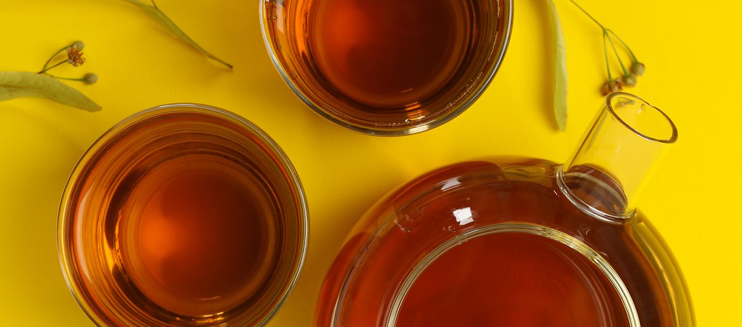 2 tazas de tila y tetera con tila de cristal transparente sobre una mesa de color amarillo