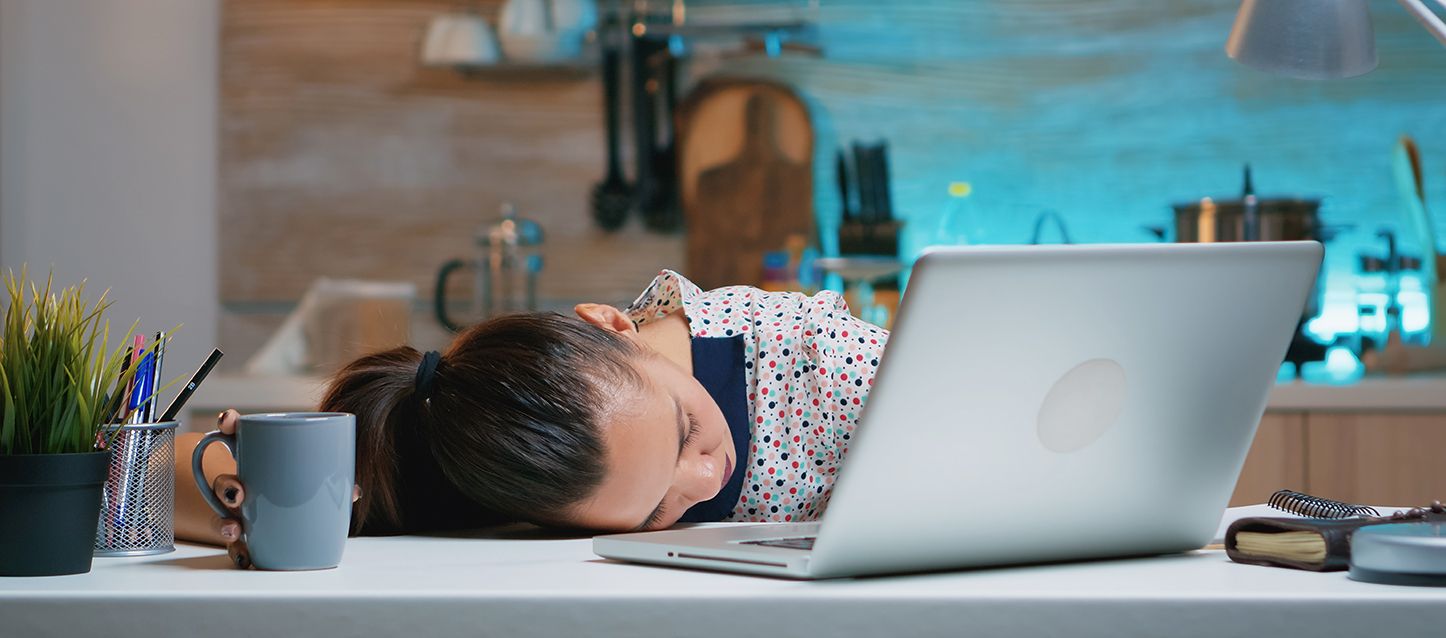 chica morena con coleta dormida en el escritorio delante del laptop cogiendo una taza