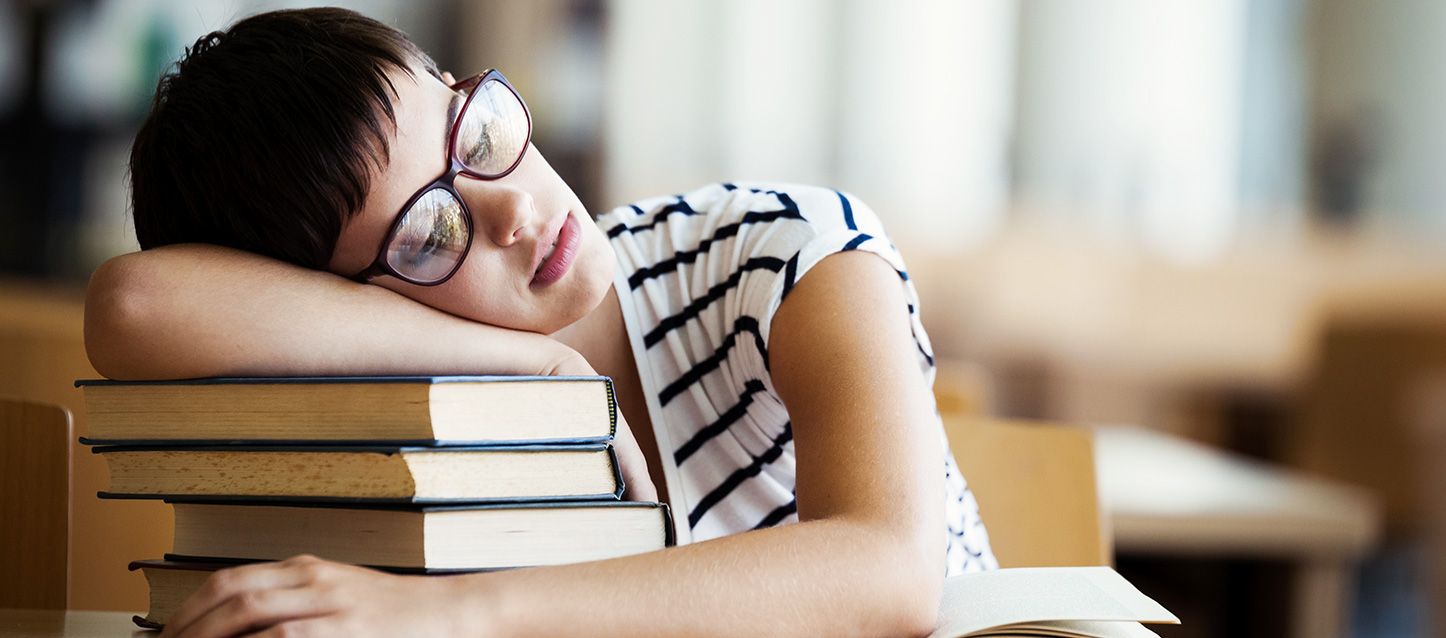 Remedios naturales para la narcolepsia chica morena de pelo corto y gafas con camiseta blanca y rayas negras dormida apoyada sobre un monton de libros