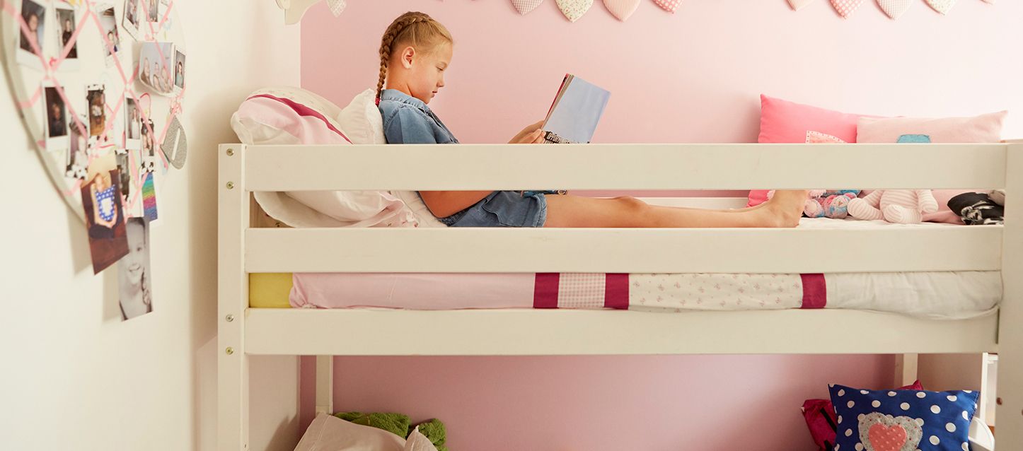Cómo poner dos camas en una habitación pequeña niña de coletas rubias leyendo en la cama de arriba de una litera