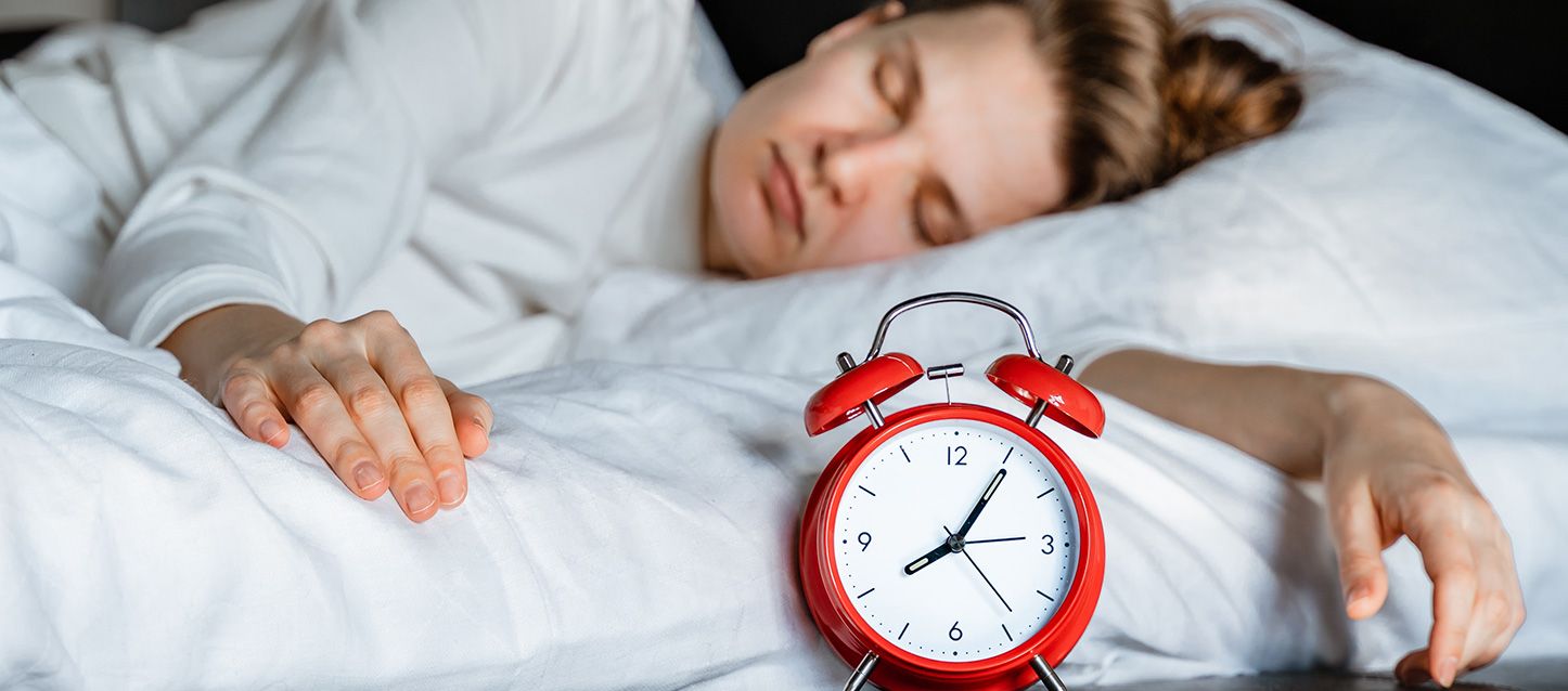 sueño por bloques mujer con pijama blanco durmiendo y un despertado rojo