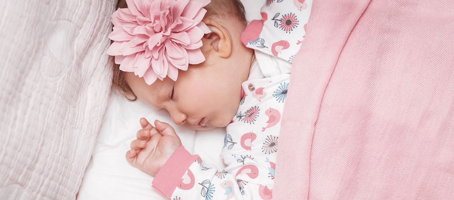 Apneas del sueño en bebés bebé durmiendo boca arriba con pijama blanco y rosa, una flor decorativa en la cabeza y tapada con manta rosa