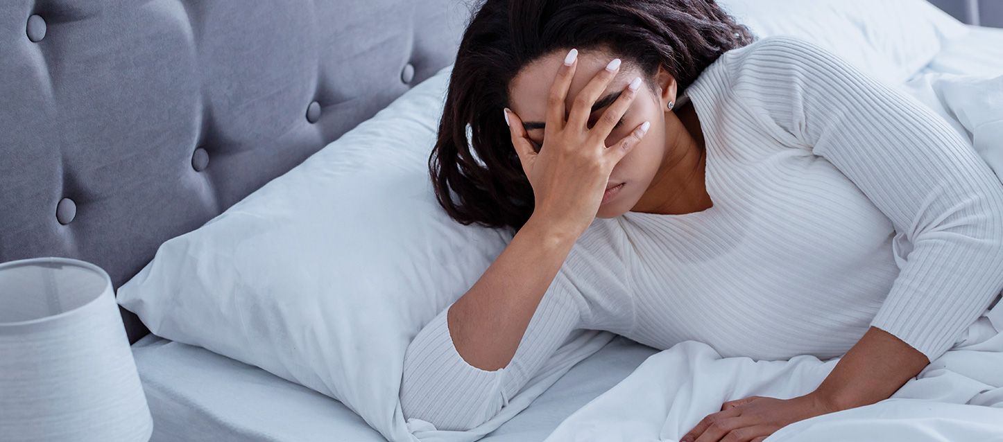 chica morena de pelo largo dentro de la cama con la mano en la cara con gesto de molestia por sueño intermitente