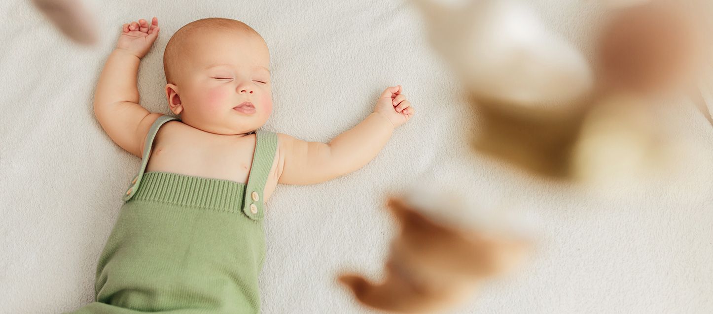 bebé durmiendo profundamente con pijama de tirantes verde sobre una cama