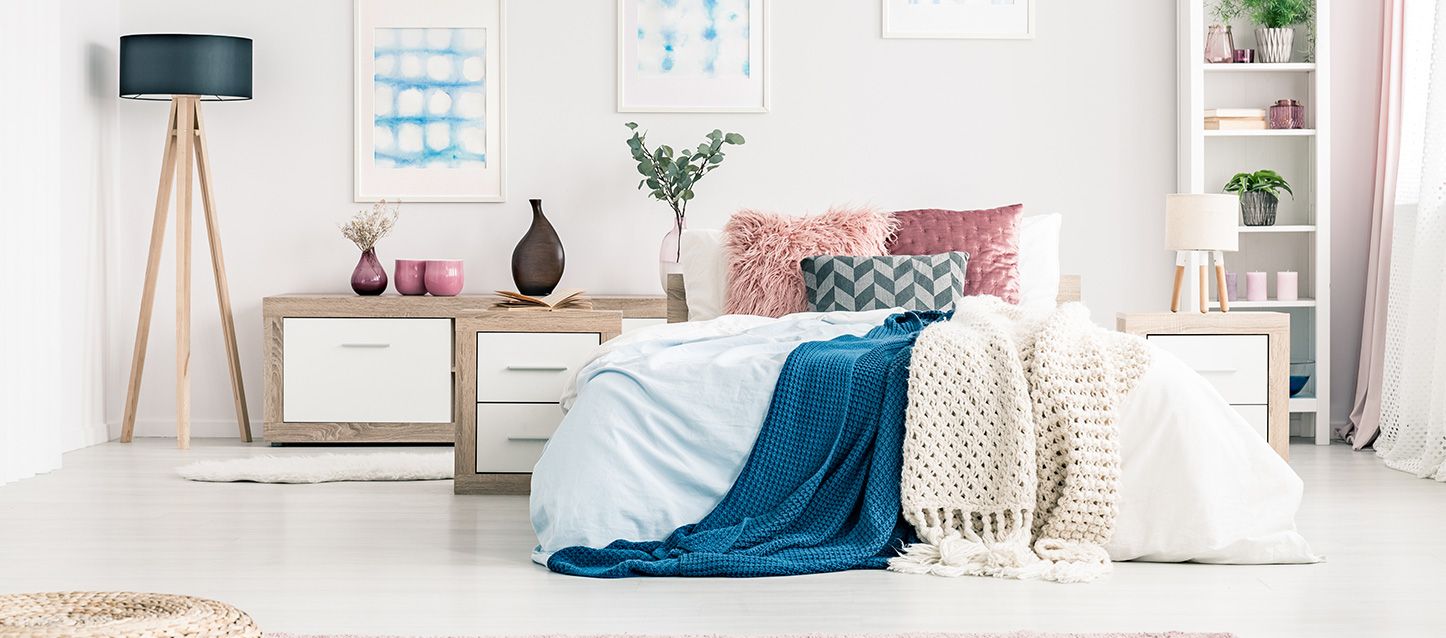 dormitorio fresco y luminoso, cama con edredon azul y manta de punto, cojines rosas, estanteria con objetos decorativos
