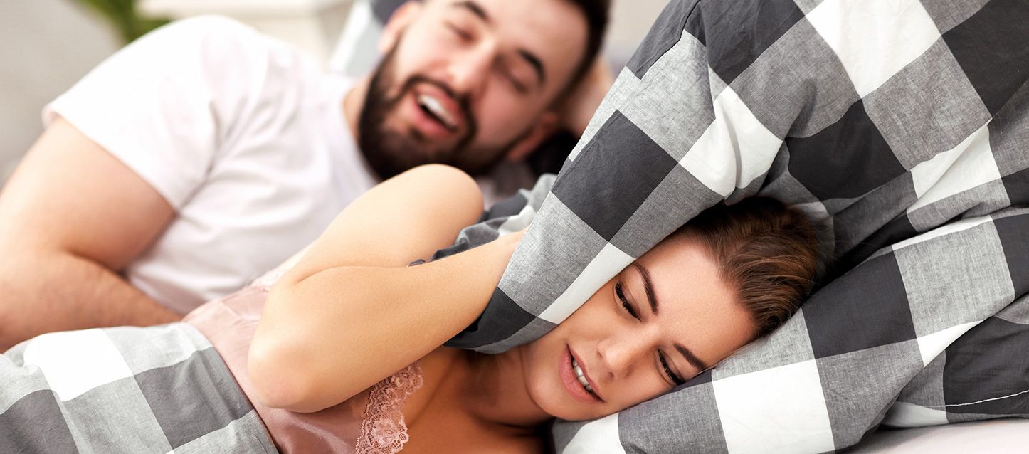 ronquidos pareja metida en la cama donde el ronca y ella se tapa los oídos con la almohada con gesto de malestar
