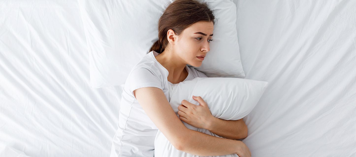 chica sobre una cama de sábanas blancas abrazada a la almohada
