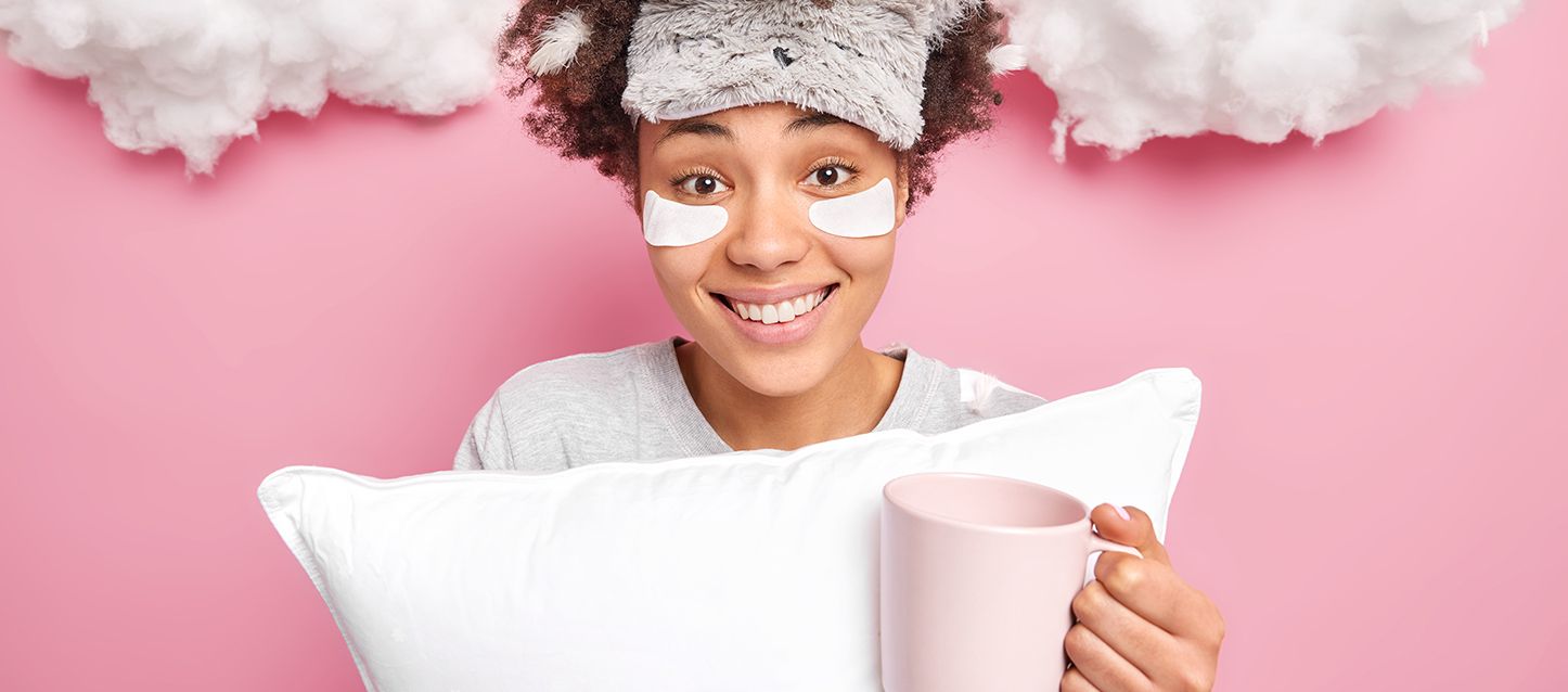 blog-2-1 chica morena con antifaz en la cabeza sujetando una almohada y una taza rosa