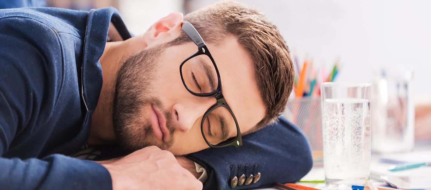 chico con gafas dormido en su mesa de trabajo delante de un vaso de agua