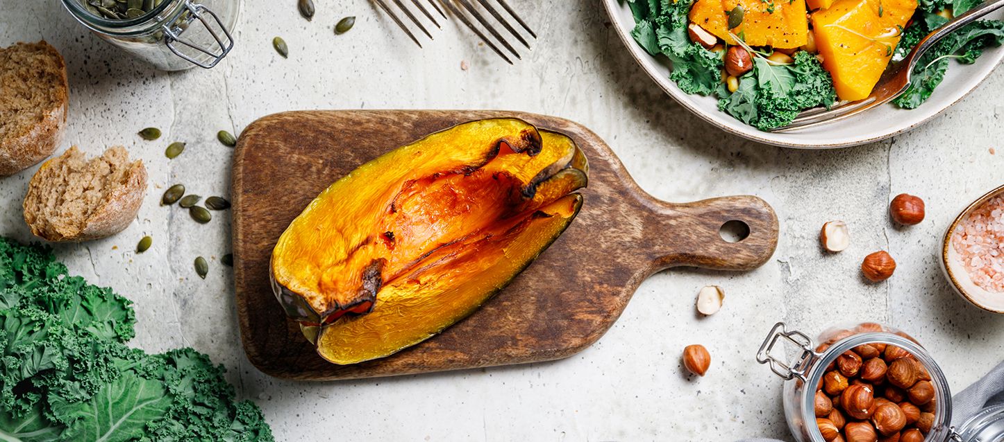 blog-1 trozo de calabaza al horno sobre una tabla de madera en una mesa con frutos secos y vegetales