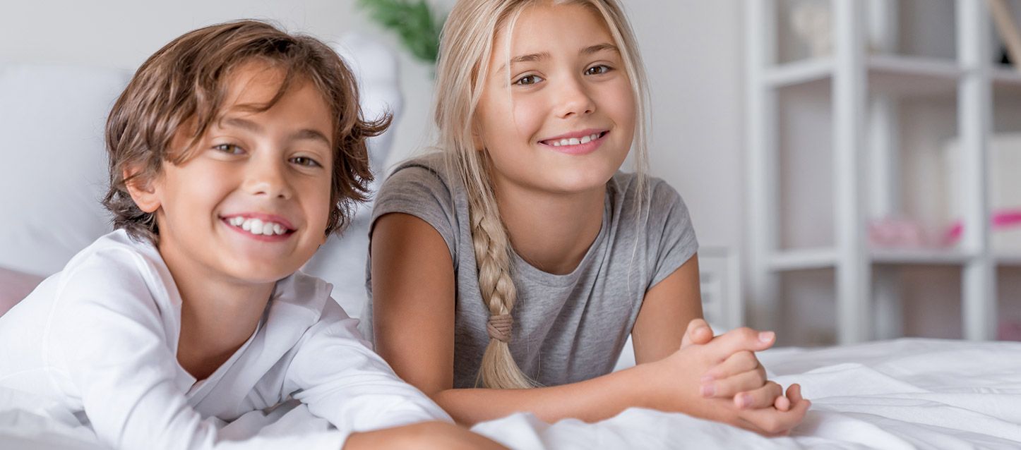 dos niños tumbados en la cama sonriendo mirando a la cámara