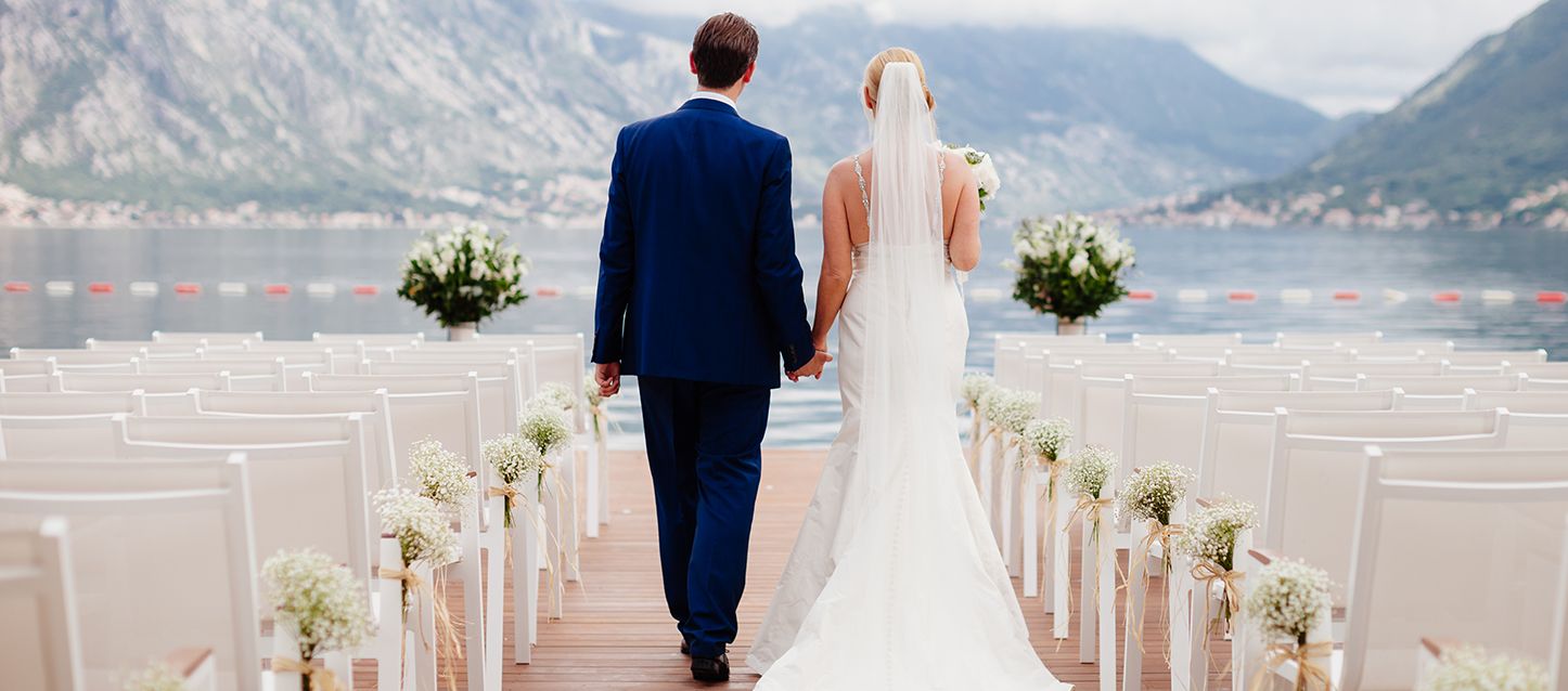Pareja de novios andando en el lugar dónde se casan rodeados de sillas y frente a un gran lago