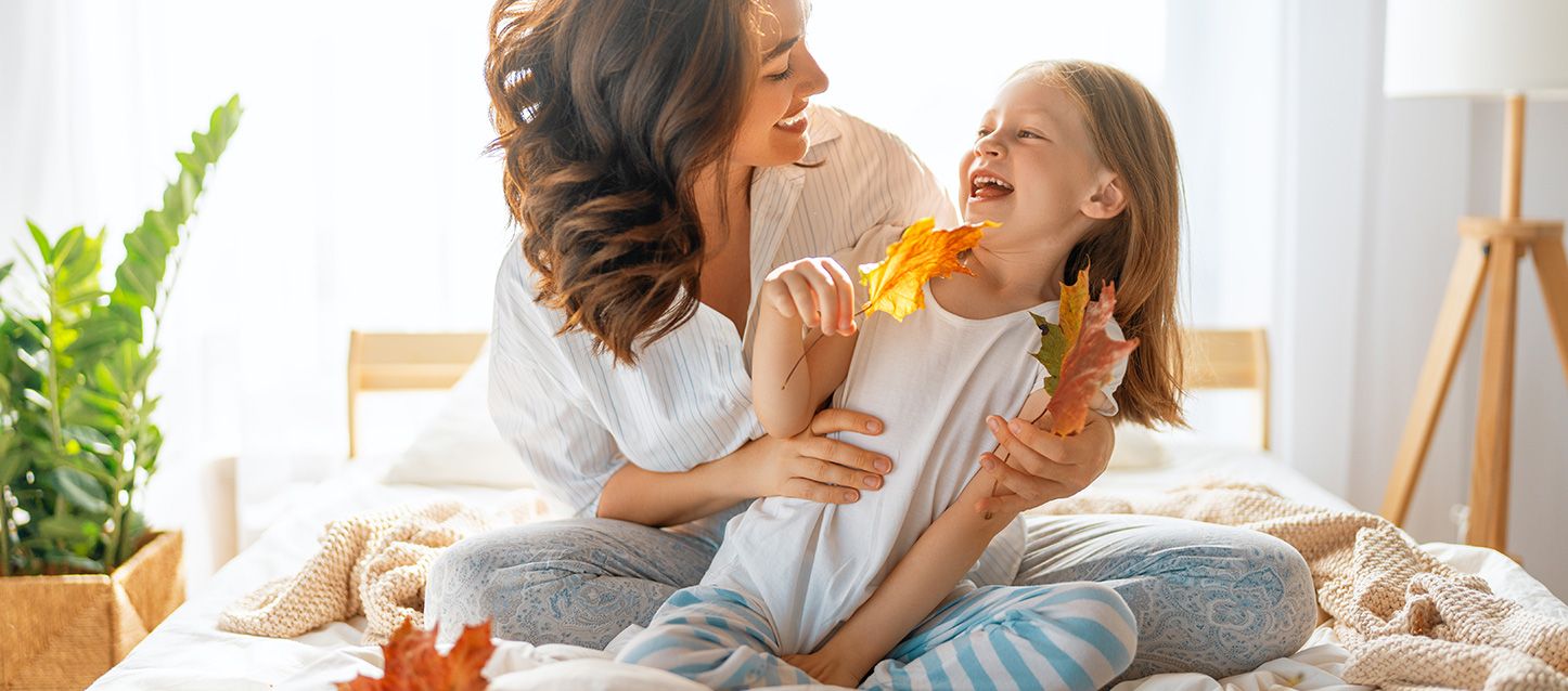 blog-1 Madre e hija sentadas en la cama riendo jugando con hojas secas de árboles