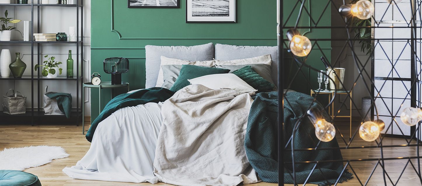 Dormitorio tipo loft con cama con sabanas grises y manta y cojines verdes, mesita de noche y estanteria
