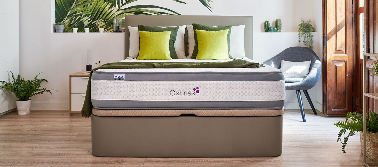Habitación con el suelo de madera, canapé, colchón oximax, dos almohadas y 4 cojines de colores amarillo y verde con cabecero gros, sillón a la derecha y mesita a la izquierda
