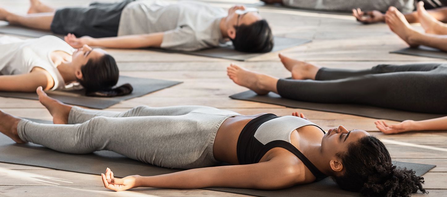 blog-1 6 personas tumbadas boca arriba en el suelo sobre una esterilla con los ojos cerrados practicando yoga nidra