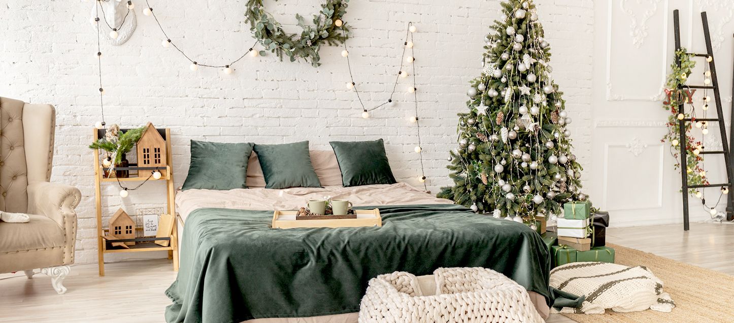 Habitación modo loft con cama y sillón con decoración navideña, árbol y regalos.