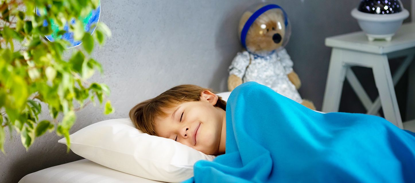 Niño durmiendo en la cama de lado sonriente tapado con manta azul