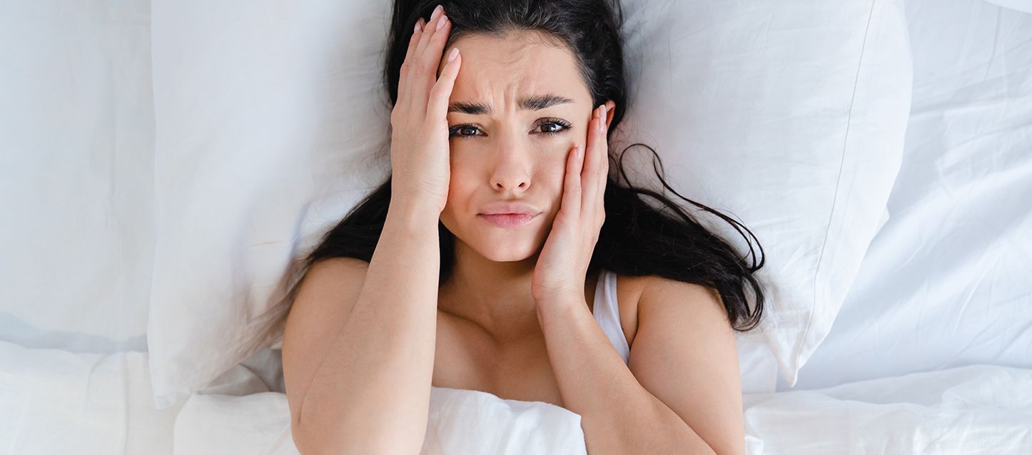 Las pesadillas más comunes conoce sus significados Chica de pelo largo negro metida en la cama cogiendo su cara con las dos manos con cara de asustada