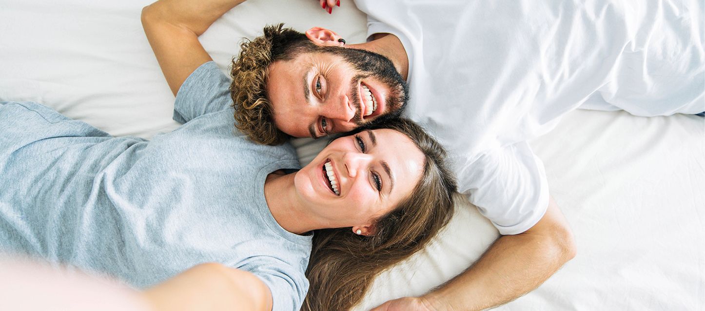 Pareja tumbada boca arriba en la cama en sentido opuesto pero con las cabezas a la misma altura