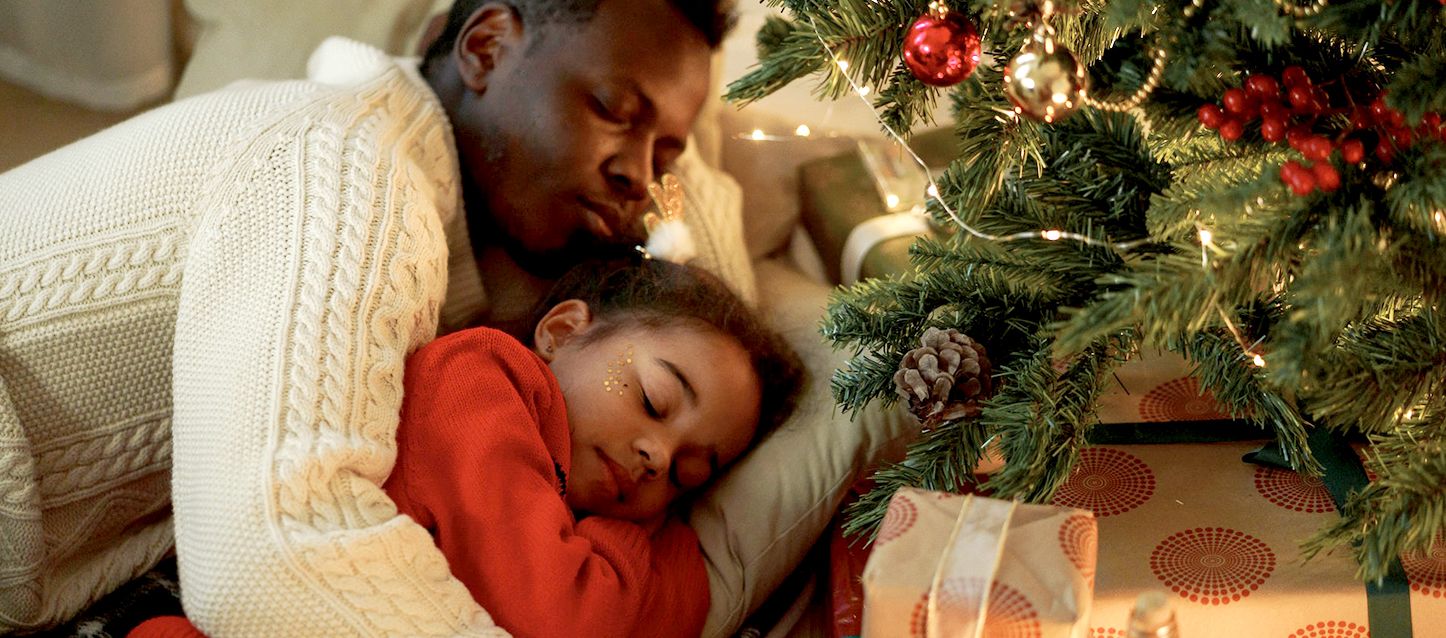Los sueños más comunes en Navidad padre e hija durmiendo abrazados en el sofá junto al árbol de navidad