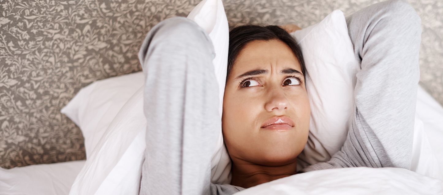 mujer tumbada boca arriba en la cama despierta mirando hacia un lado hacia arriba con gesto de desaprobación