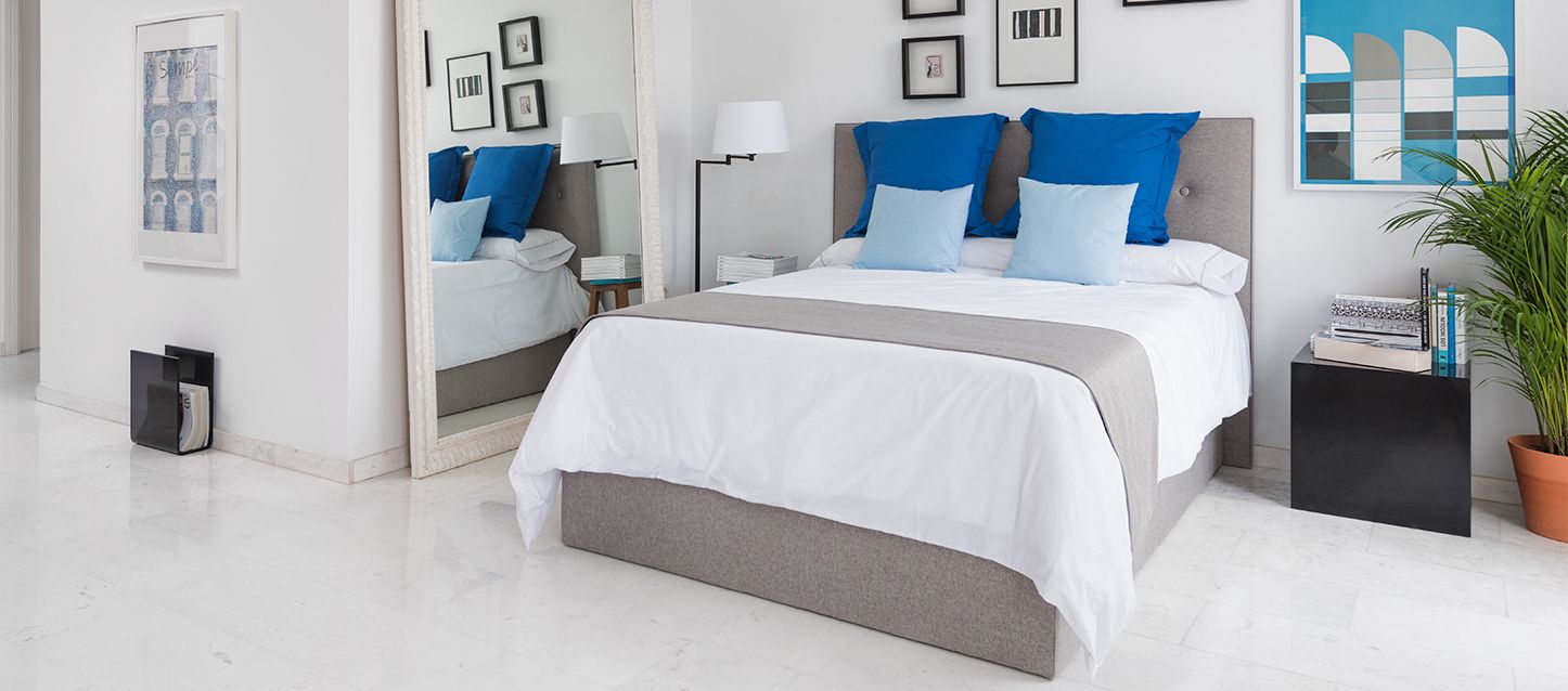 Espejos en el dormitorio Habitación con una cama, almohada y cojines, mesita de noche con libros y espejo a la derecha y espejo en la parte izquierda