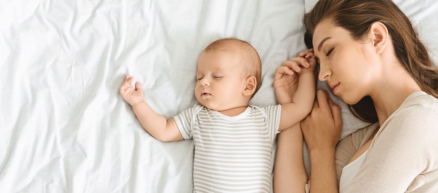 Un bebe con un pijama a rayas durmiendo junto a su madre en una cama